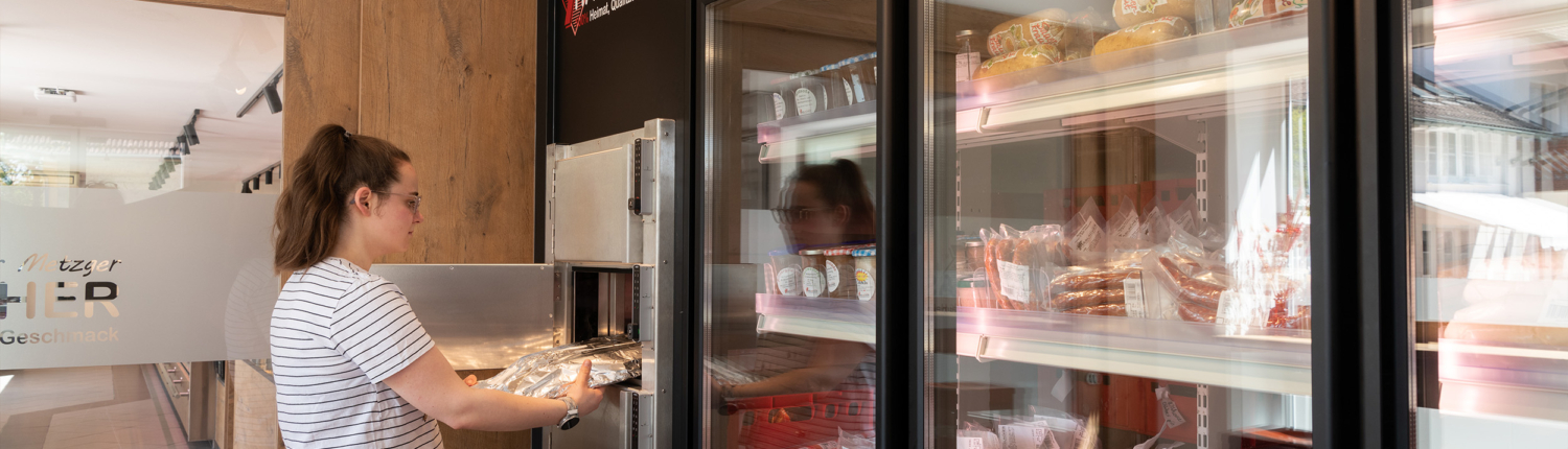 Eine Dame holt ihre Ware im 24-Stunden Hybrid Laden, der in der Metzgerei integriert ist ab